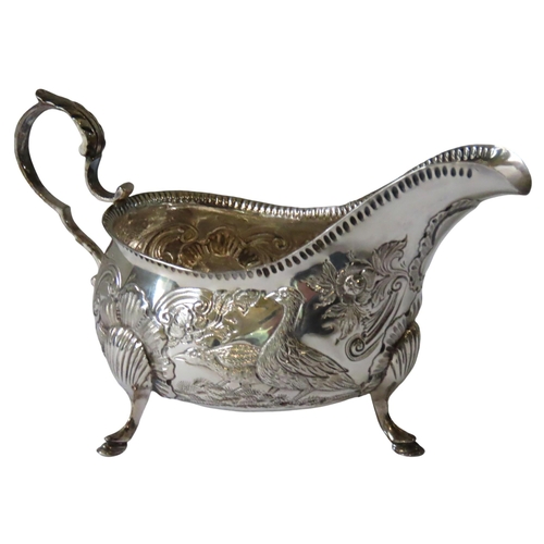 667 - AN ORNATE VINTAGE IRISH SILVER SAUCEBOAT, the sides with ornate repousse decoration depicting grouse... 