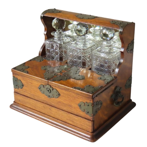 215 - A LATE VICTORIAN OAK TANTALUS, holding three square form cut glass decanters within a mirror backed ... 