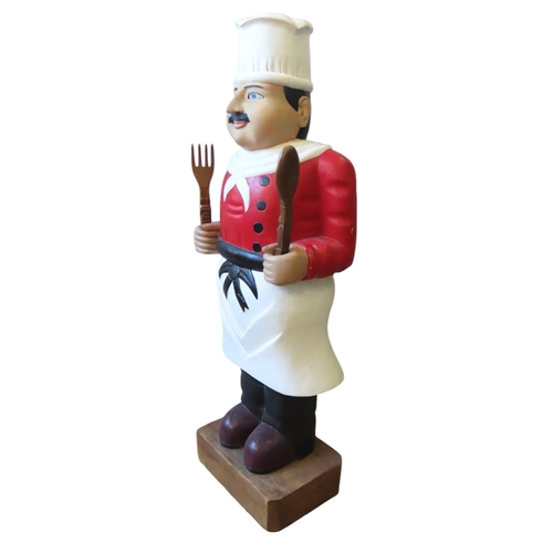 454 - A PAINTED HARDWOOD FIGURE OF A CHEF, modelled standing, holding a spoon and fork, raised on a rectan... 