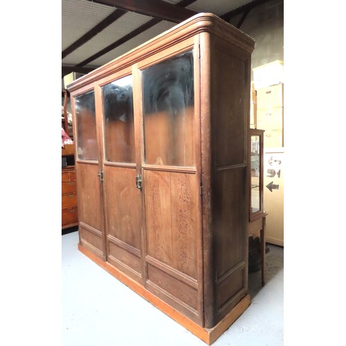 25 - A LARGE PINE BIBLIOTHEQUE, ogee cornice over three part glazed cabinet doors, raised on a plinth bas... 