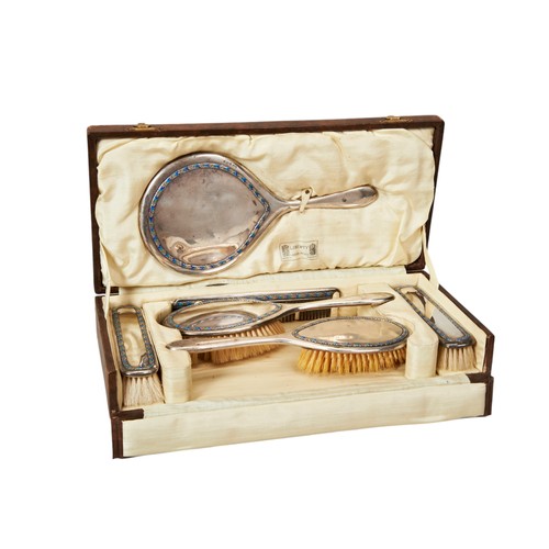 A LIBERTY & CO. SILVER SIX PIECE VANITY SET, each piece decorated with bands of enamelled leaf decoration, presented in a gilt tooled tan leather transit case, inscribed 'Liberty, London-Paris, By Special Appointment' each piece marked L & C, Birmingham, 1919, the lot also includes an associated silver pot lid