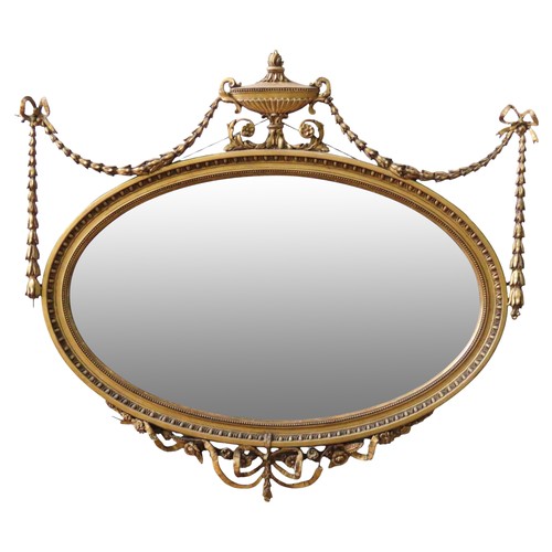 75 - AN ADAMS-STYLE GILT FRAMED MIRROR, LATE 19TH CENTURY, the oval frame surmounted by a Grecian style u... 