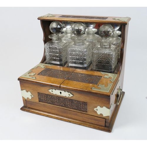 502 - Late Victorian oak tantalus, having carved guilloche detailing with nickel mounts, enclosing three h... 