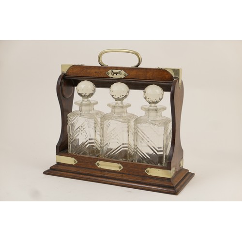 605 - George V oak three bottle tantalus, having plated brass mounts and three slice cut decanters, with k... 