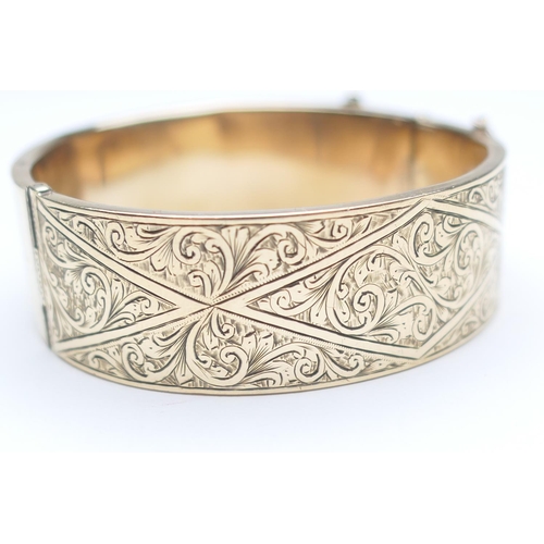 409 - 9ct gold hinged bangle, chased with foliate scrolls, with safety chain, interior size approx. 54mm, ... 