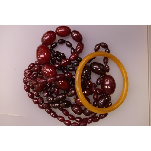 399 - Butterscotch amber bangle, weight 14.9g; also two claret amber beaded necklaces and a pair of claret... 