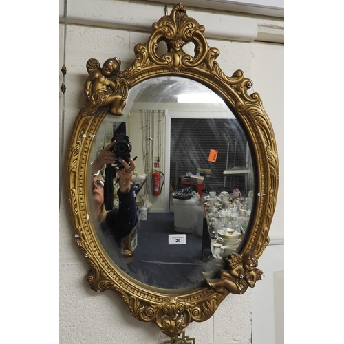 29 - Plaster form and gilt coloured oval wall mirror surmounted with cherubs