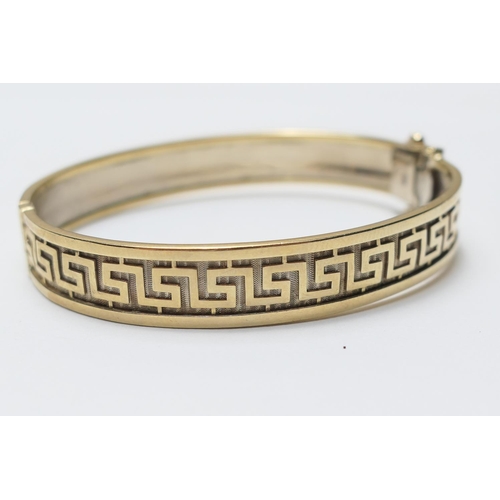 435 - 9ct two colour gold hinged bangle, having a Grecian key design against a white gold textured ground,... 