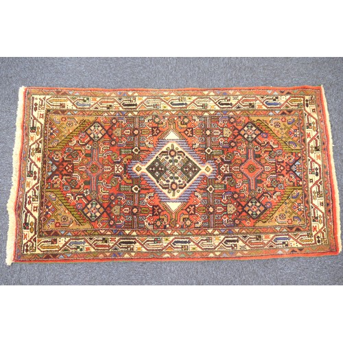 628 - Pakistani small red ground woollen rug, centred with a blue and fawn lozenge medallion, 147cm x 80cm