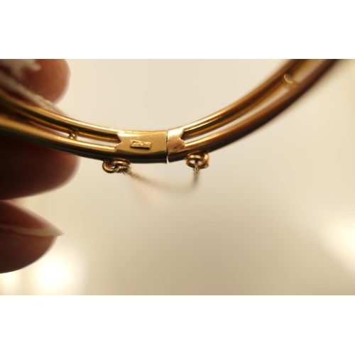 396 - 18ct gold and pearl bangle, worked with a horseshoe channel set with seed pearls and flanked with sh... 