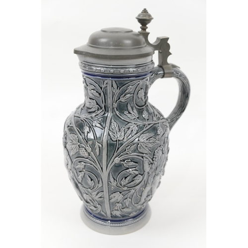 61 - Decorative German glazed pitcher, having a hinged pewter cover, the body relief moulded throughout w... 