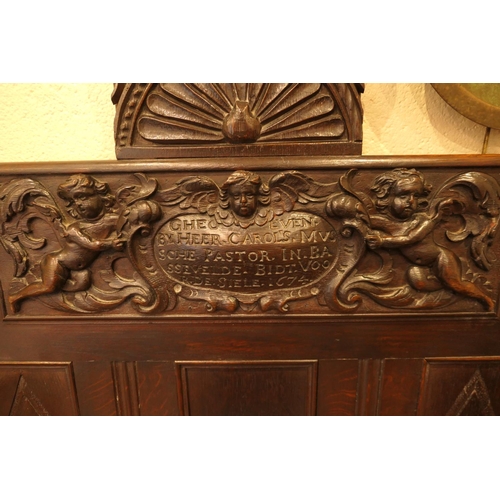 908 - Carved oak settle, the back centred with a dated carved oak panel with cherubs supporting an inscrib... 