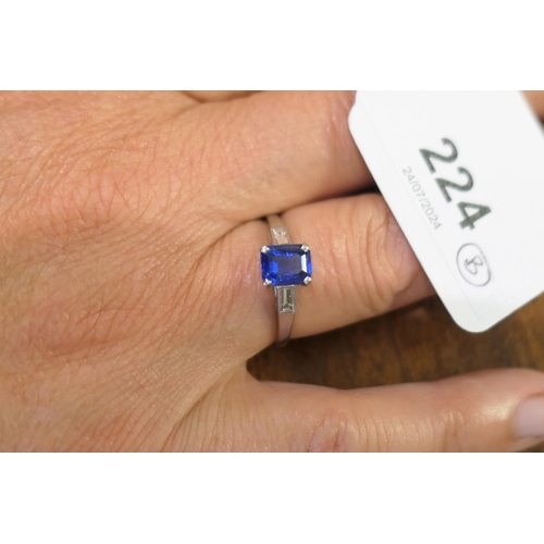 224 - Sapphire solitaire ring, emerald cut stone of approx. 1ct, in a platinum four claw mount, flanked by... 