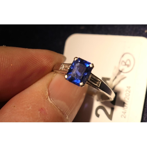 224 - Sapphire solitaire ring, emerald cut stone of approx. 1ct, in a platinum four claw mount, flanked by... 