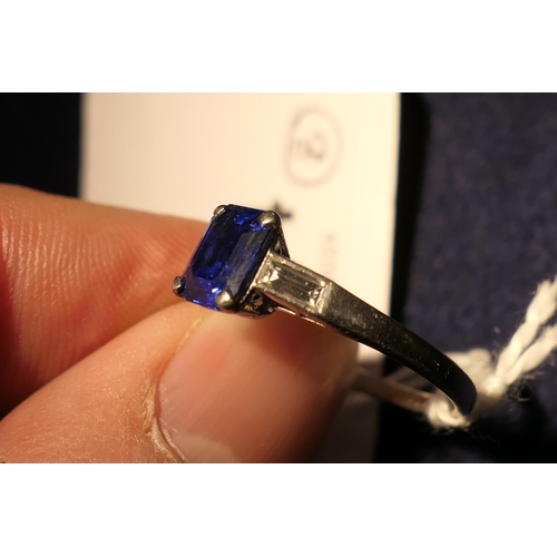 224 - Sapphire solitaire ring, emerald cut stone of approx. 1ct, in a platinum four claw mount, flanked by... 