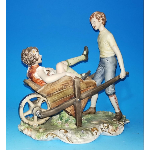 212 - A Capodimonte group: girl in wheelbarrow, wheeled by a boy