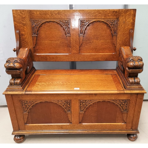 633 - An early 20th century golden oak monks bench with lion arm rests and box seat