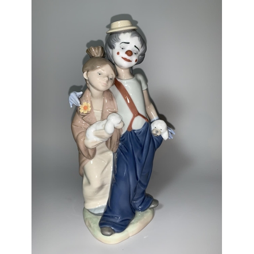 12 - A Lladro group - a young girl holding a puppy leaning against a young clown with a puppy in his pock... 