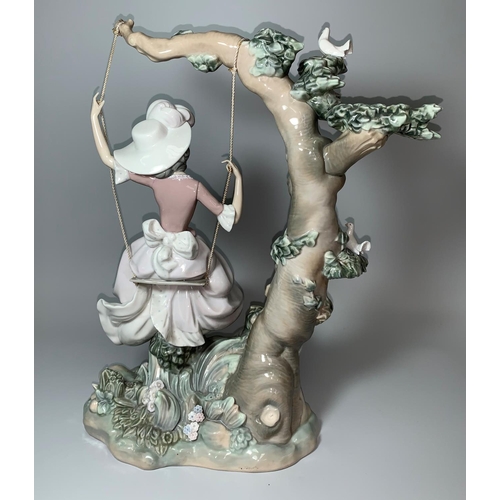 27 - A large impressive Lladro group of a girl with full skirt and feathered hat on a swing from the bran... 