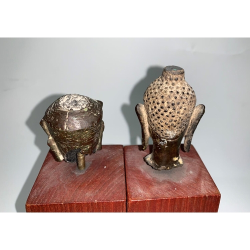 136 - Two South East Asian Buddha heads in gilt bronze, mounted on hardwood columns, 6 cm x 5 cm (1 a.f.)