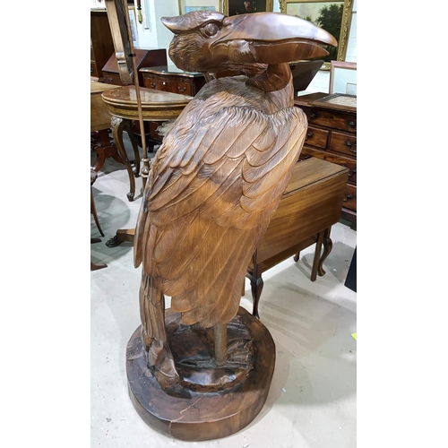 488 - A large carved wood sculpture depicting a pelican with a fish in its beak, height 128 cm