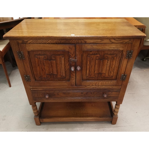 632 - A reproduction oak side cabinet with twin linen fold panel doors, drawer and underdshelf