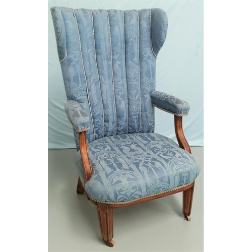 580 - A 1930s high wing back armchair in blue brocade on square tapering legs and castors