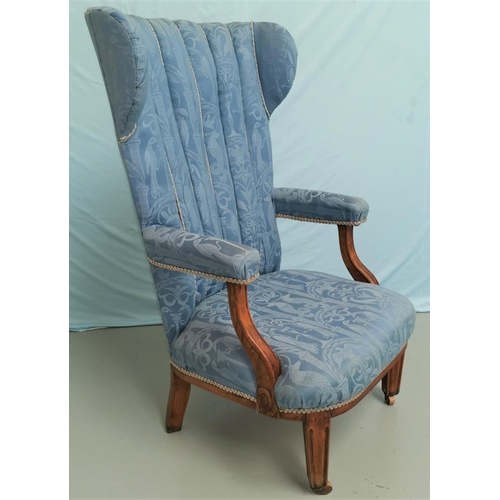 580 - A 1930s high wing back armchair in blue brocade on square tapering legs and castors