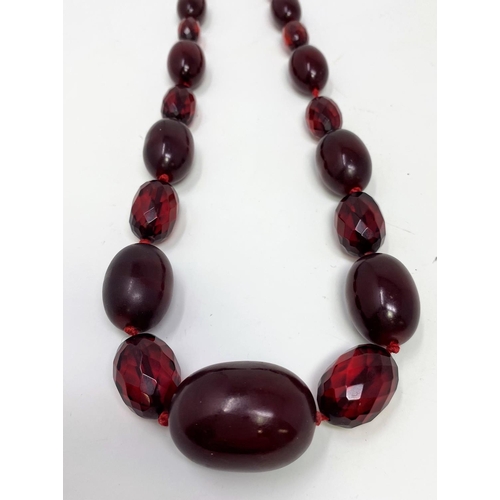 423 - A cherry amber Bakelite colour necklace with alternating cloudy oval beads and clear faceted beads, ... 