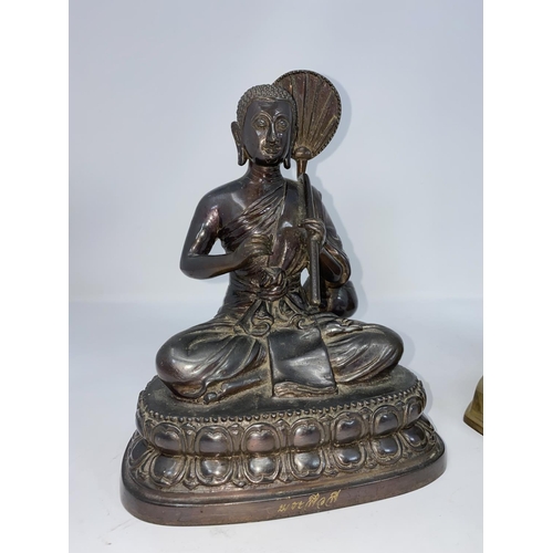 115 - An oriental bronzed Buddha figure in seated lotus position holding a leaf fan,  and a similar metal ... 