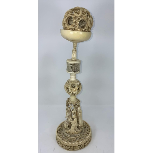 97 - A 19th century carved ivory puzzle ball on stand with base of carved dragons, the pillar with figure... 