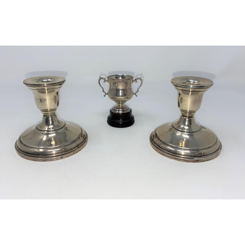 323 - A pair of sterling silver candlesticks; a hallmarked silver small trophy cup, 1 oz