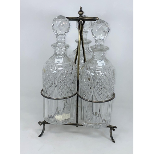 202 - An Arts & Crafts silver plated triple decanter stand with 3 cut bottles