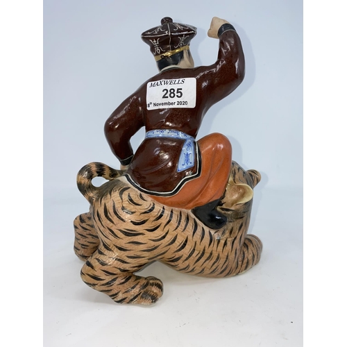 285 - A Chinese ceramic figure of man seated on a tiger holding its tail, unmarked, height 21.5cm