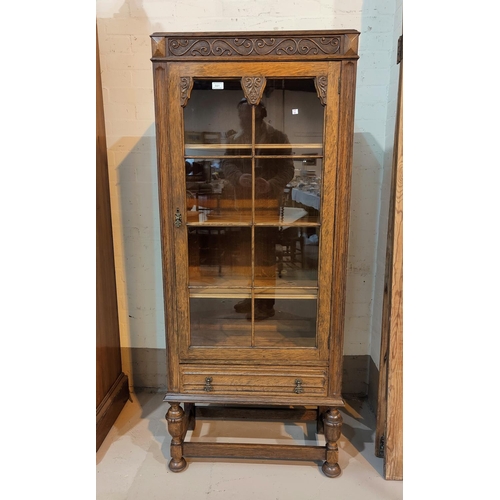 551 - A 1930's golden oak display cabinet, tall and narrow, with carved decoration, single glazed door and... 