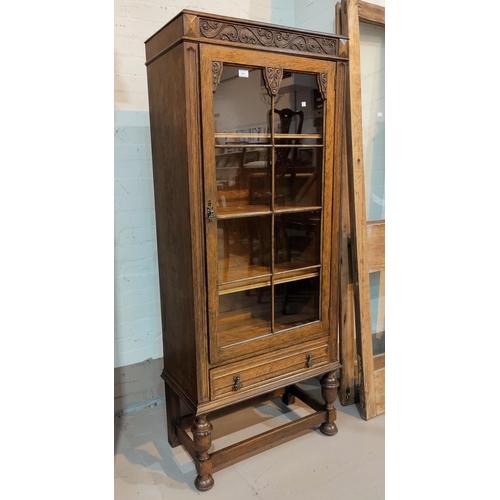 551 - A 1930's golden oak display cabinet, tall and narrow, with carved decoration, single glazed door and... 