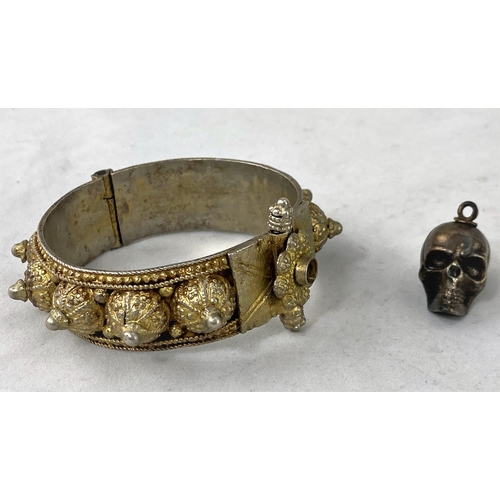 344 - An unusual skull pendant containing miniature dice; a Middle Eastern hinged bangle in ornate white m... 