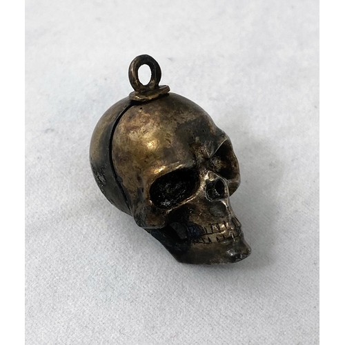 344 - An unusual skull pendant containing miniature dice; a Middle Eastern hinged bangle in ornate white m... 