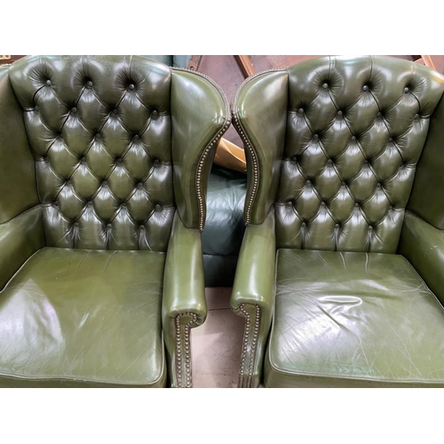 509 - A pair of gentleman's leather wing back armchairs with deep button backs, studded borders in green, ... 