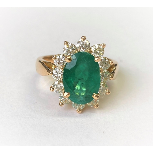 418 - An 18ct gold dress ring set with a large faceted oval emerald, 11mm x 7mm and surrounded by 12 diamo... 