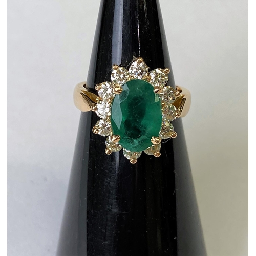 418 - An 18ct gold dress ring set with a large faceted oval emerald, 11mm x 7mm and surrounded by 12 diamo... 