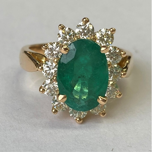 418 - An 18ct gold dress ring set with a large faceted oval emerald, 11mm x 7mm and surrounded by 12 diamo... 