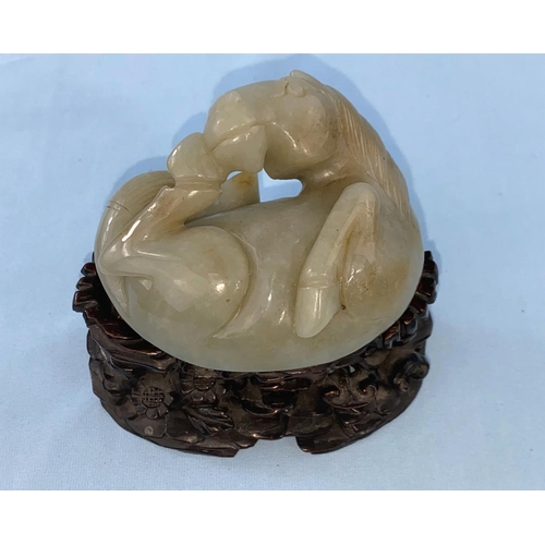 336 - A Chinese jade coloured hardstone carving of a foal curled up on associated intricately carved woode... 