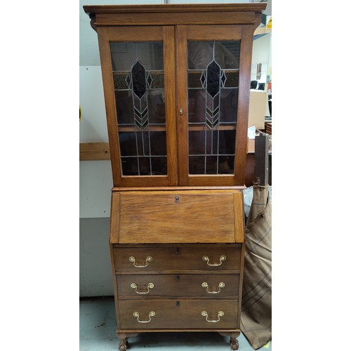 653A - A golden oak leaded coloured glass bureau bookcase with drop front and three drawers bellow on ball ... 