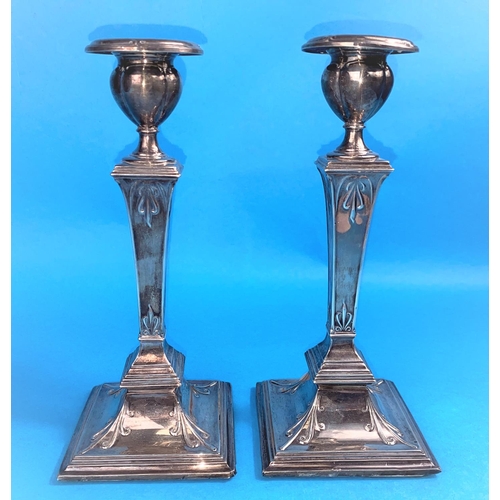 571 - A hallmarked silver pair of candlesticks with square columns, scrolled decoration and weighted bases... 
