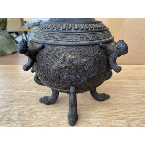353b - A Japanese bronze lidded pot on three dragon head feet, the lid with child holding large ball, chara... 