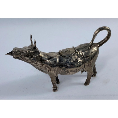 642 - A continental white metal cow creamer with relief chased decoration, the top filling aperture hinged... 