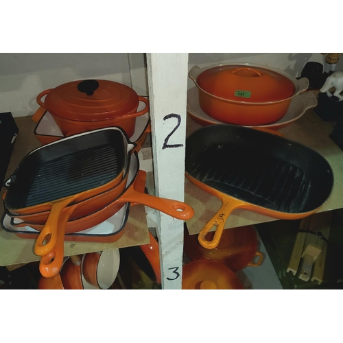 143 - A selection of Le Creuset and similar style cast metal cooking ware in orange, with a wooden pan sta... 