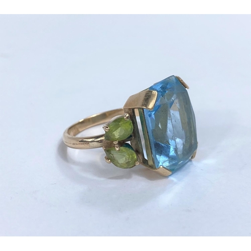 678E - A large dress ring set with rectangular clear blue stone, possibly blue topaz, flanked by 2 peridot ... 