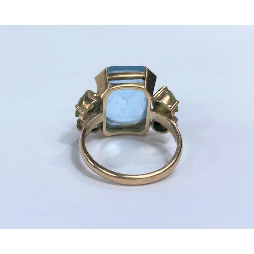 678E - A large dress ring set with rectangular clear blue stone, possibly blue topaz, flanked by 2 peridot ... 
